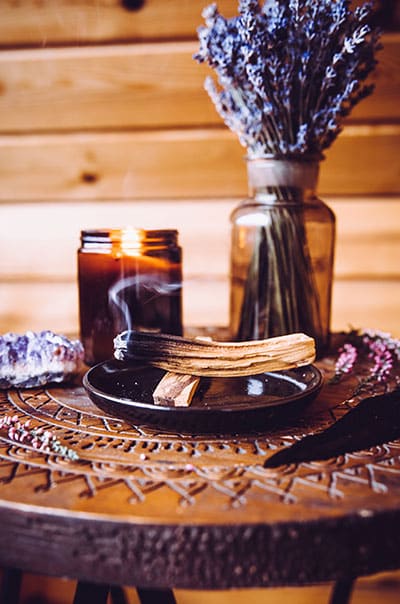 A metaphysical supply store table with a candle, burning Palo Santo, a crystal, and lavender.