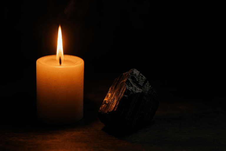 A candle burning in the dark beside a piece of black tourmaline.